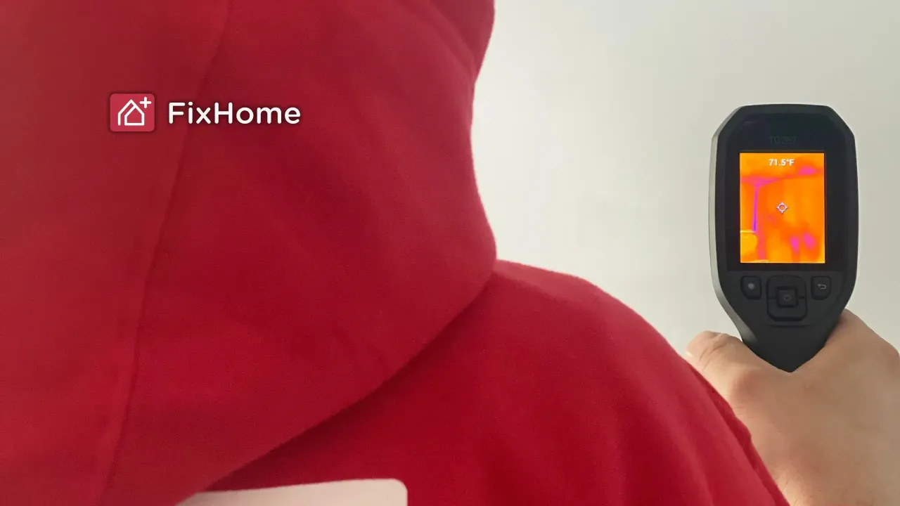 A person in a red hoodie using a thermal camera to inspect a wall