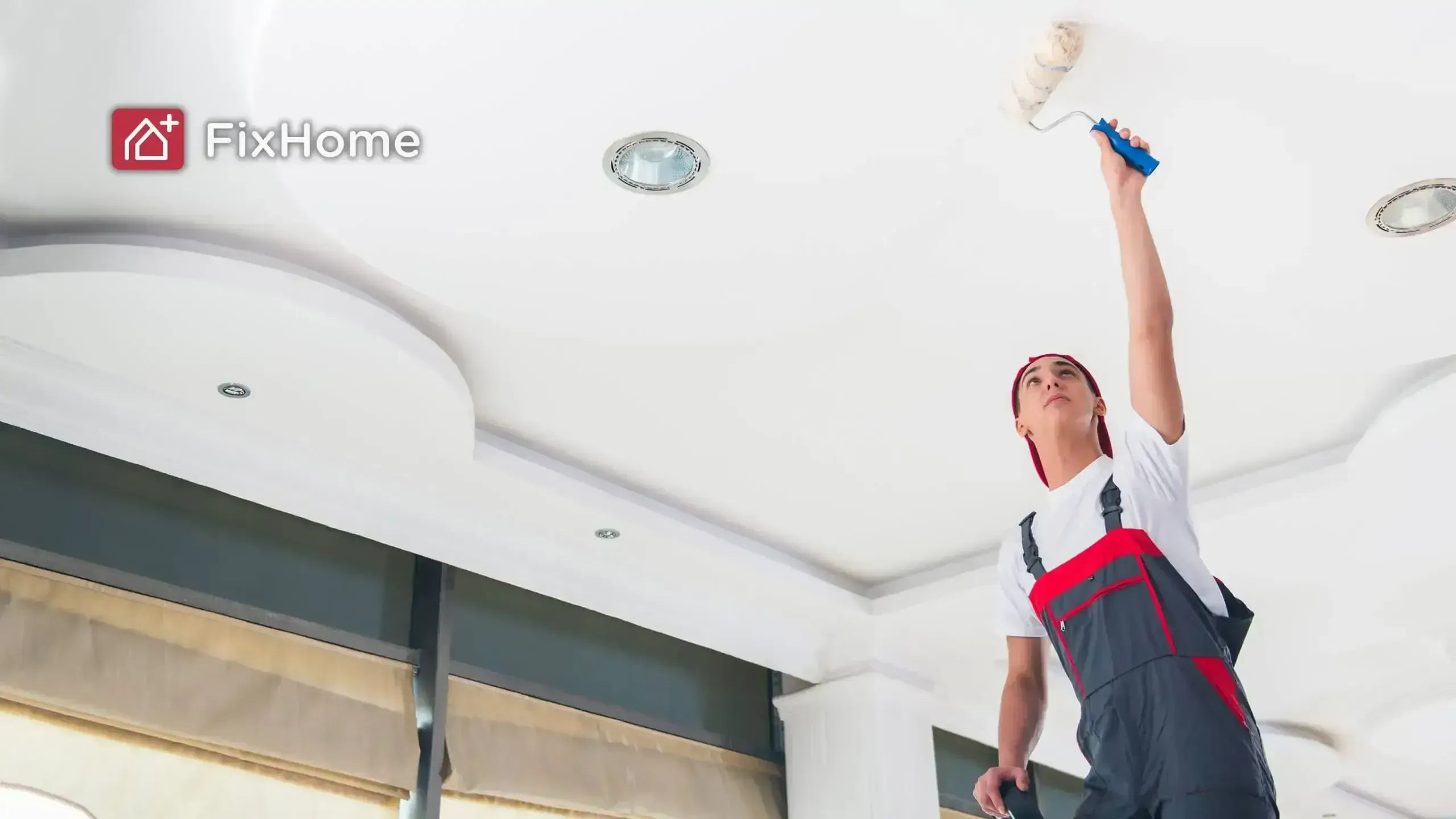 Painter in red and gray overalls using a roller to paint a ceiling.