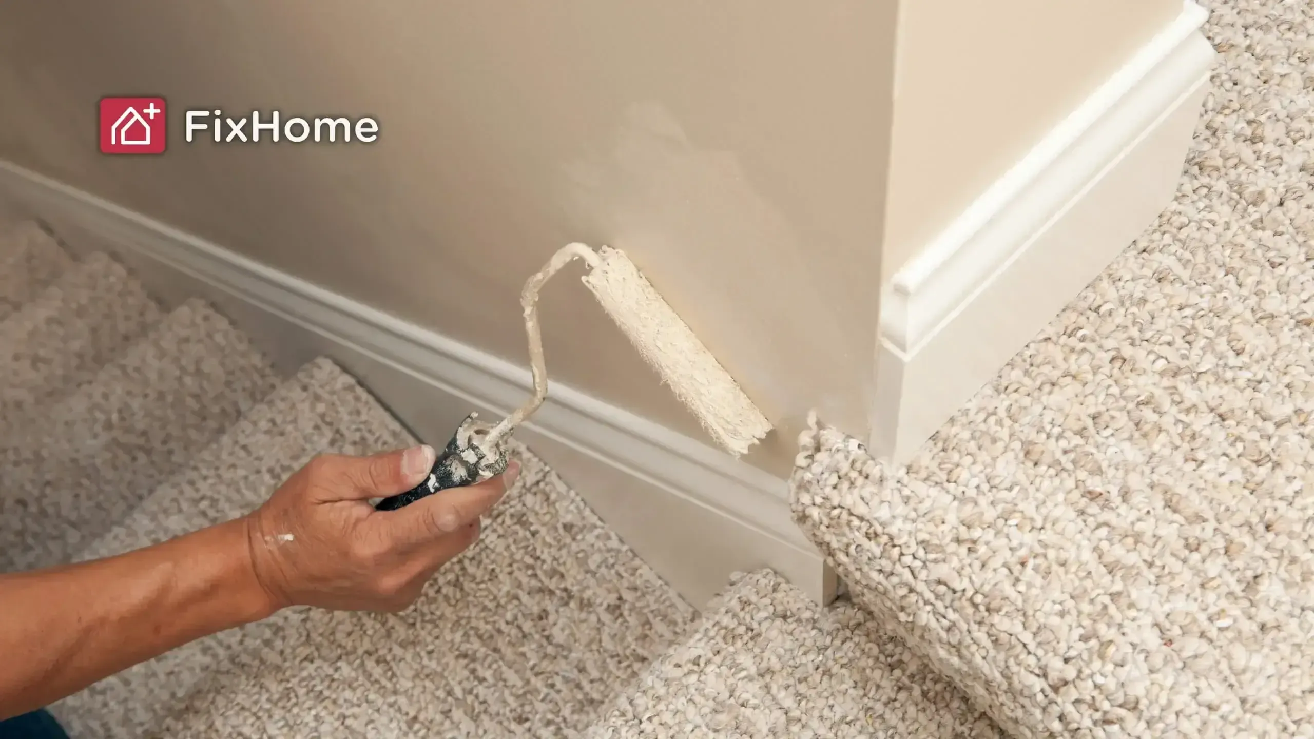 A hand holds a small paint roller, painting the riser of a carpeted staircase white