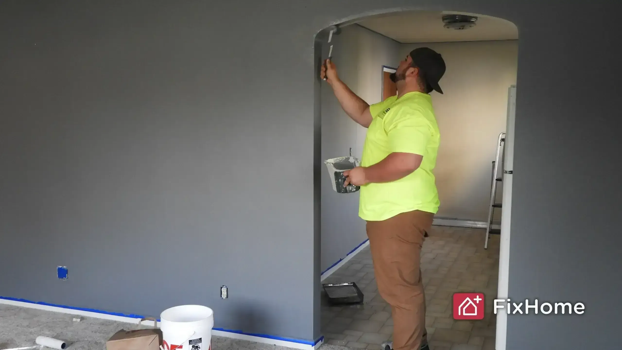 Person painting a gray wall near an arched doorway