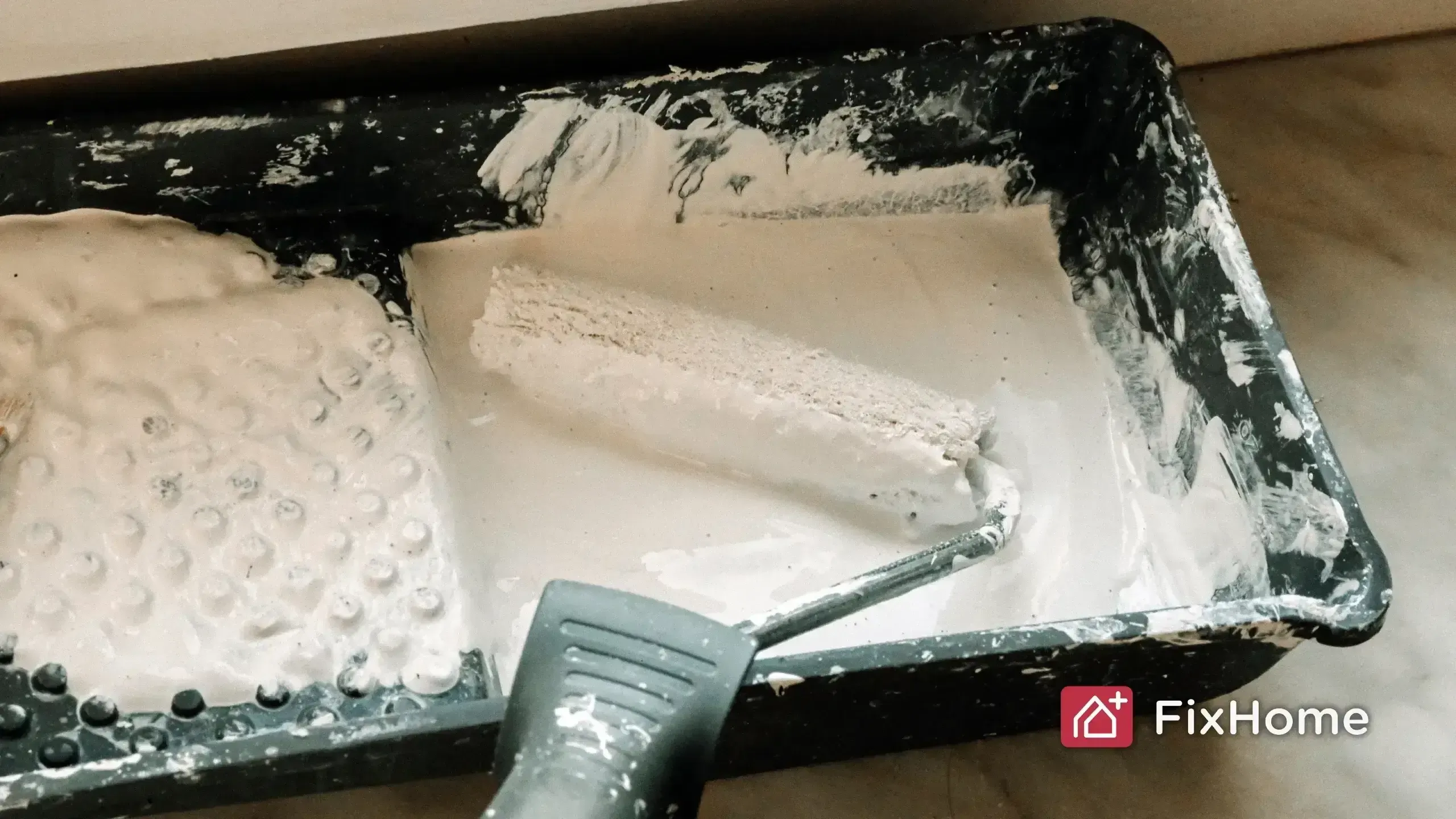 Paint tray with a roller partially covered in white paint
