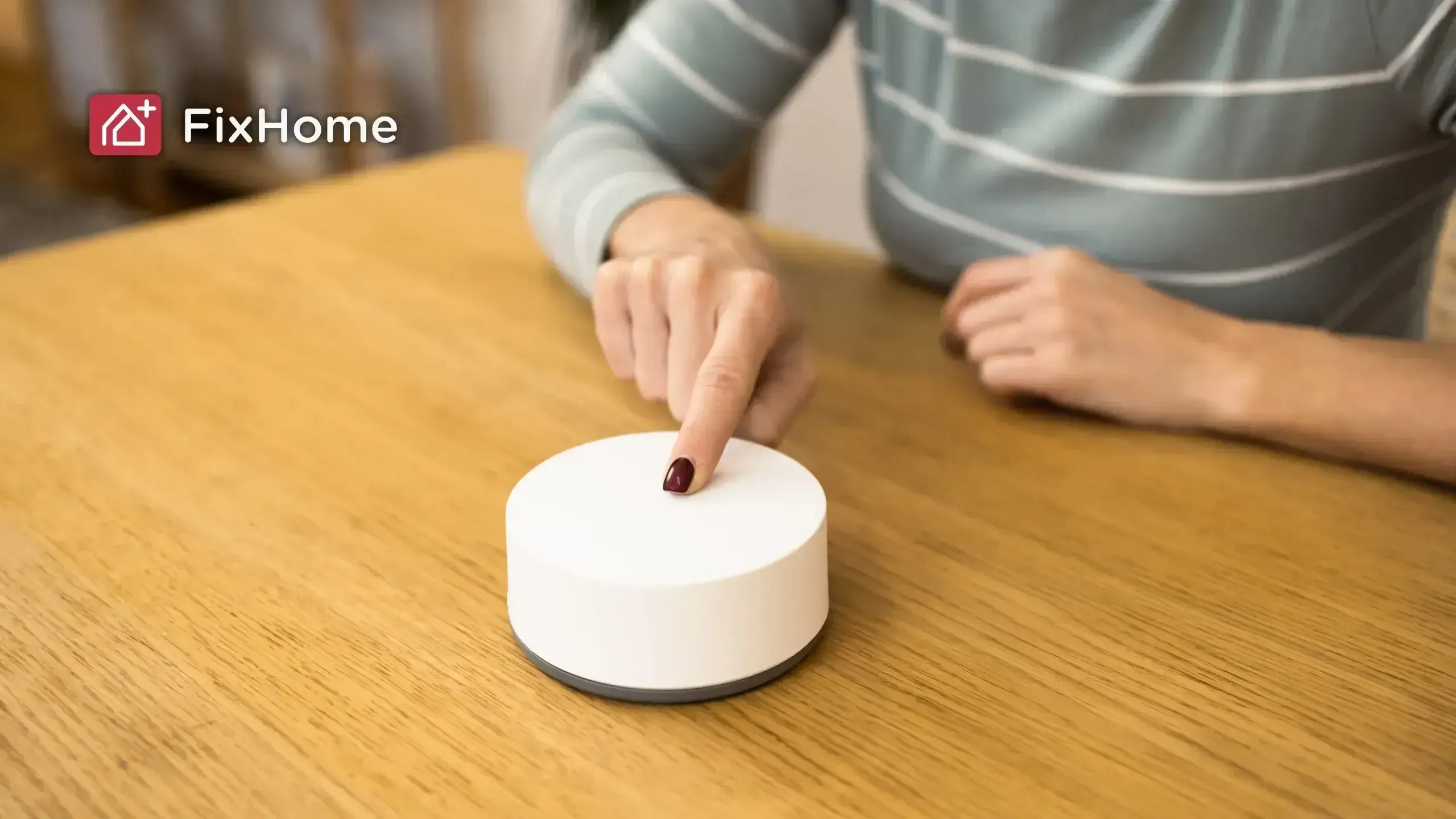 Hand pointing at a white circular smart home device on a wooden table