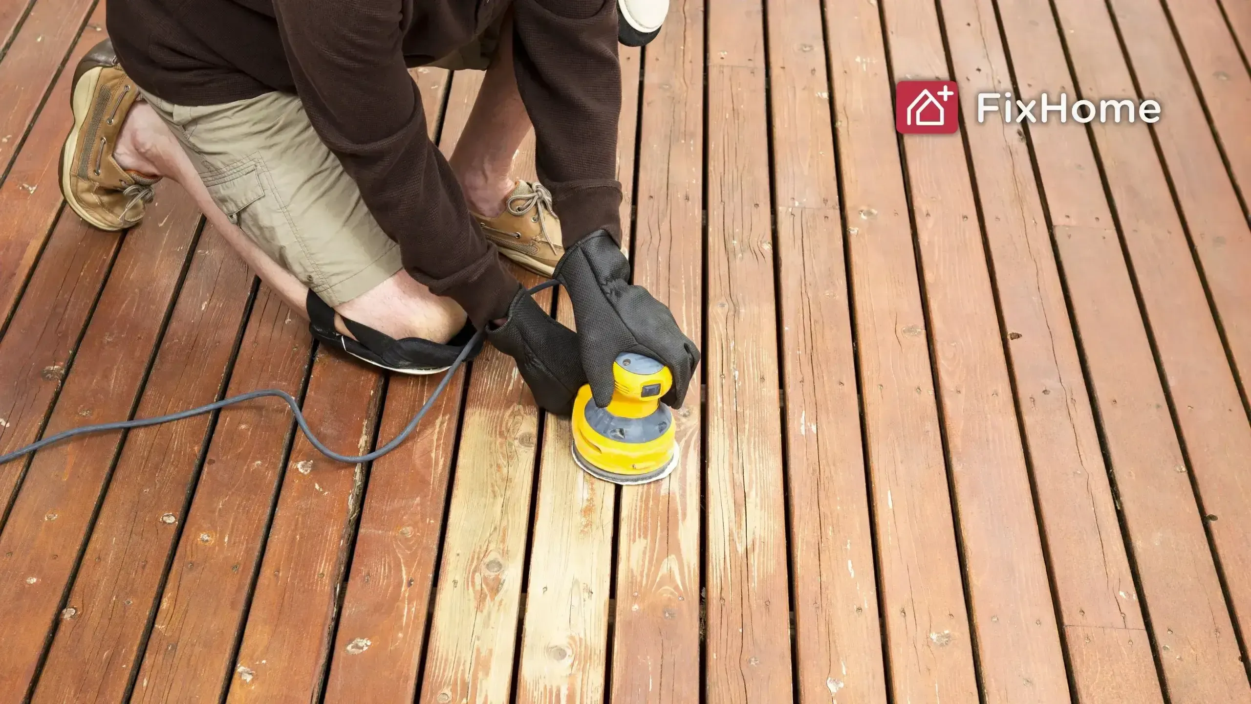 A person in gloves is using a yellow sander on a wooden deck floor.