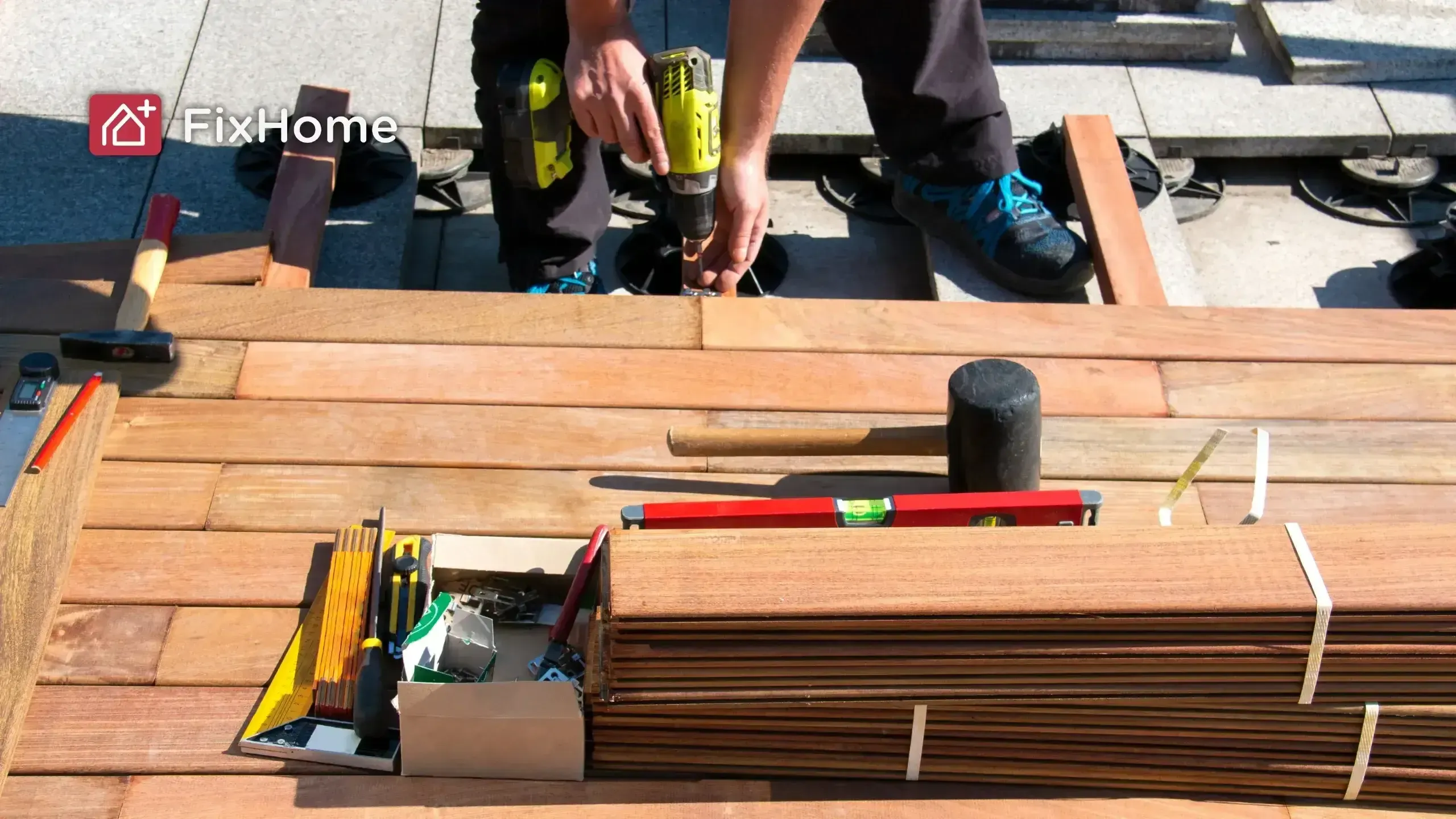 A person uses a drill while working on wooden deck planks, with tools organized nearby