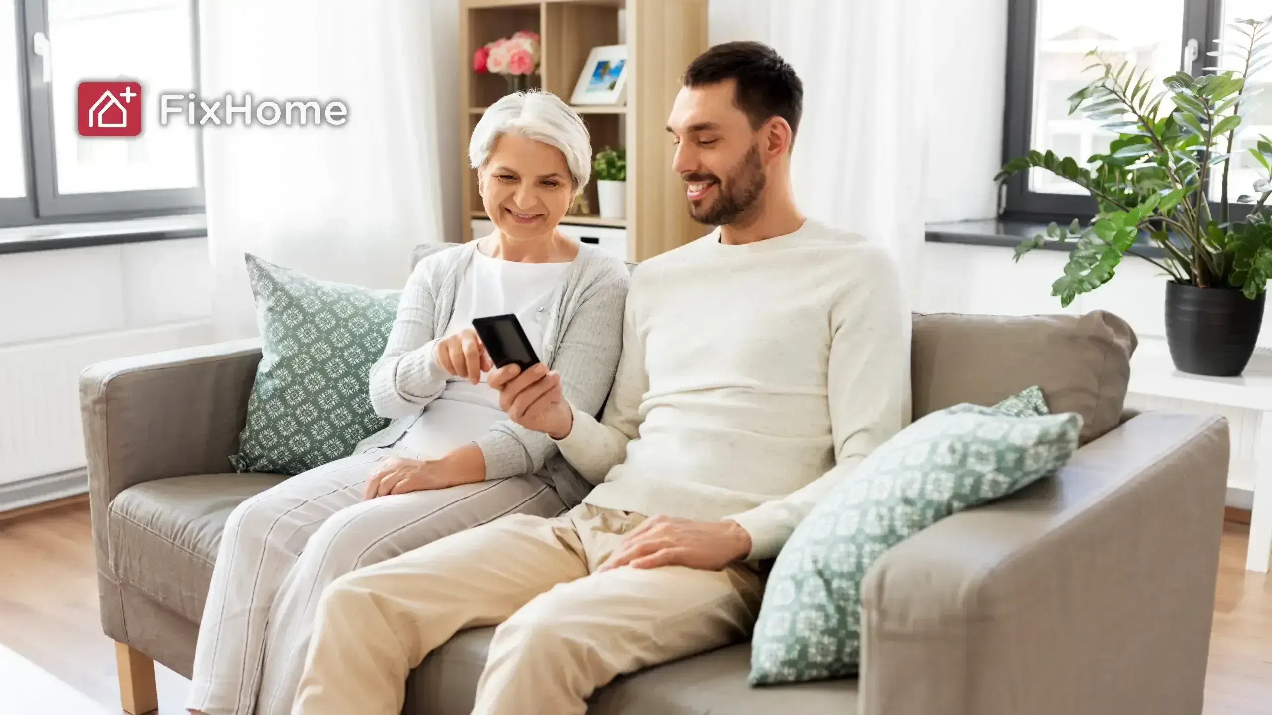 A smiling older woman and her son are sitting on a couch, sharing a smartphone