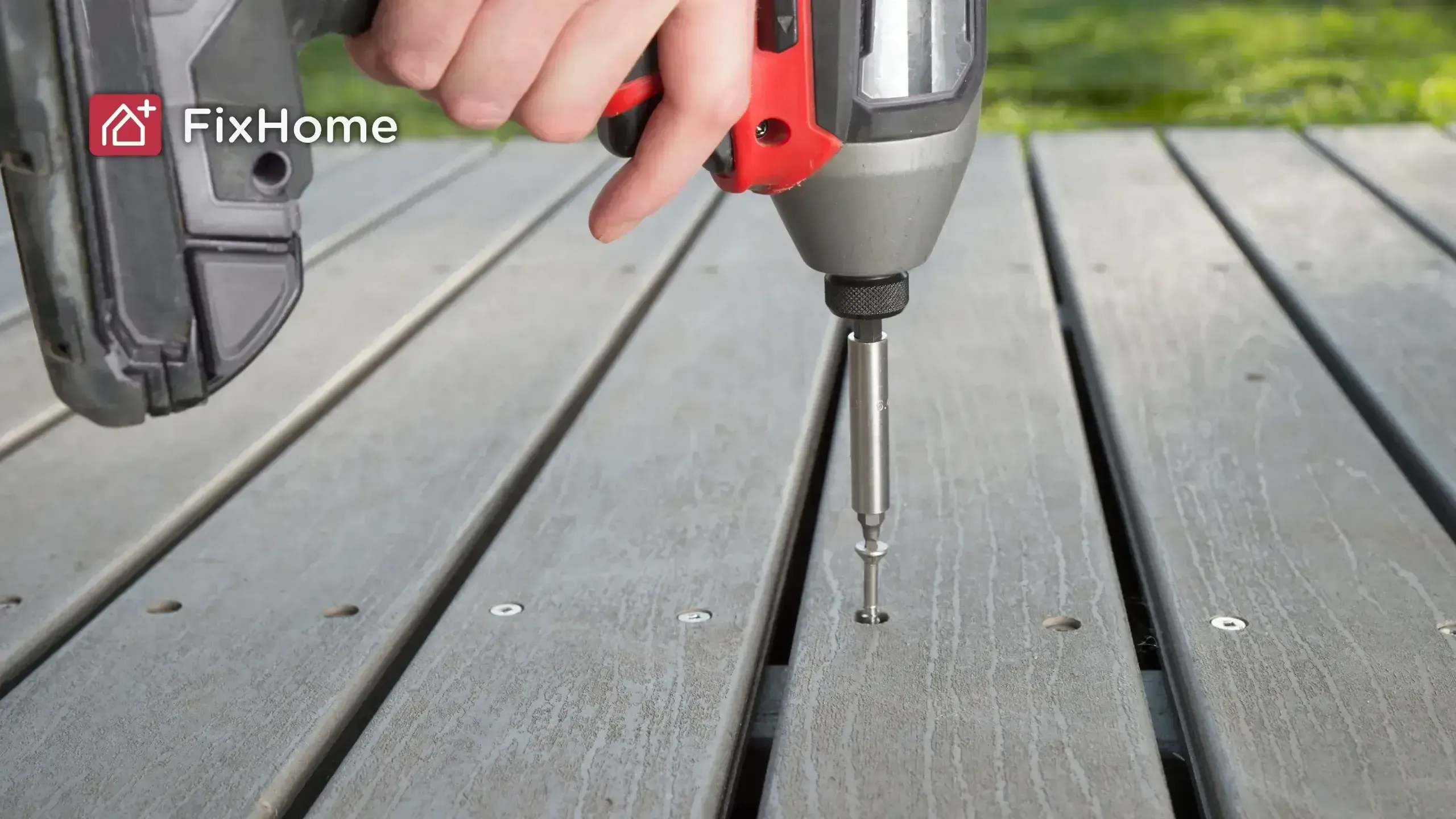 A hand holding a power screwdriver, driving a screw into wooden decking.