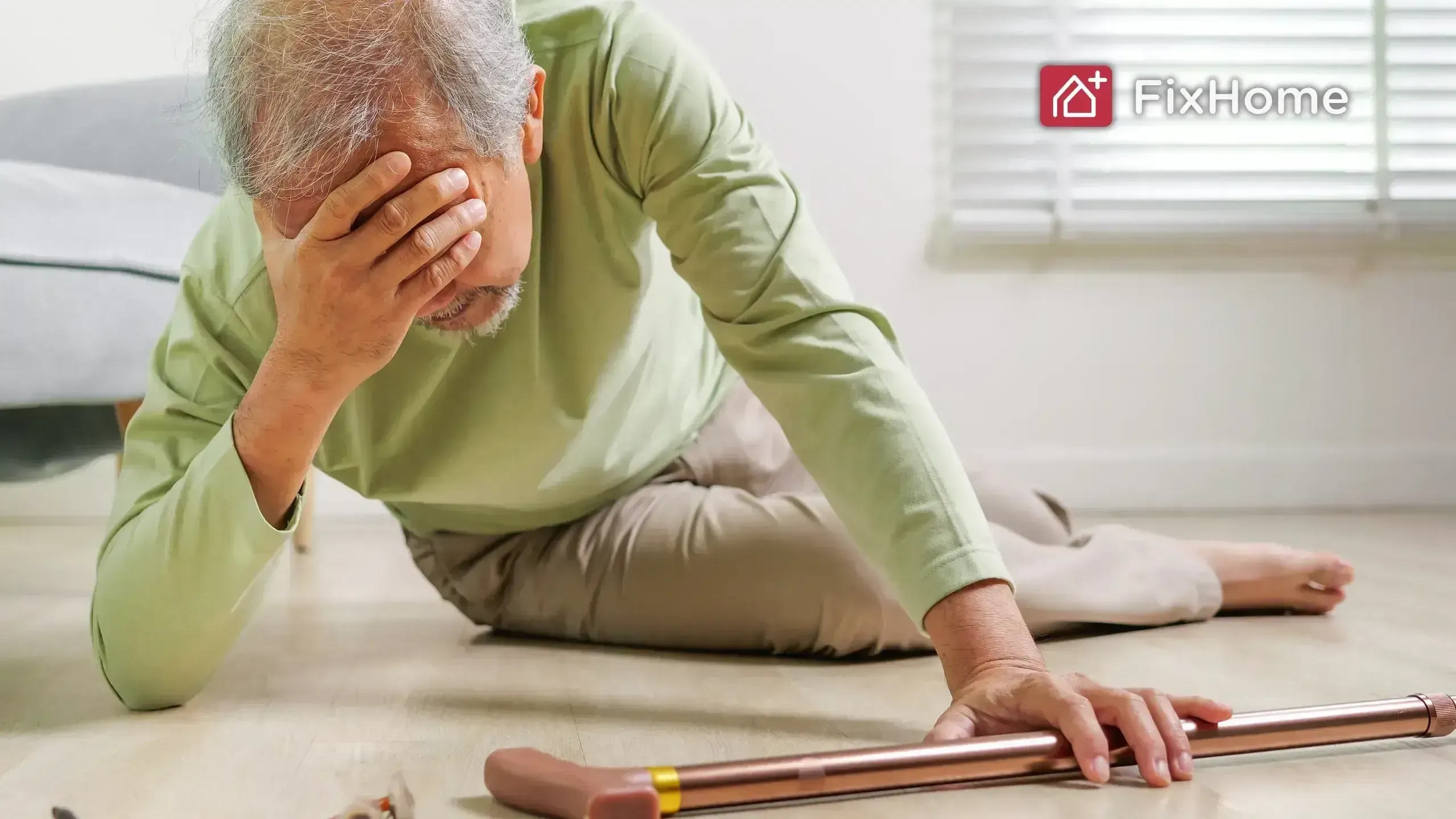 A fall elderly man is on the floor, holding his head in distress, with a cane nearby