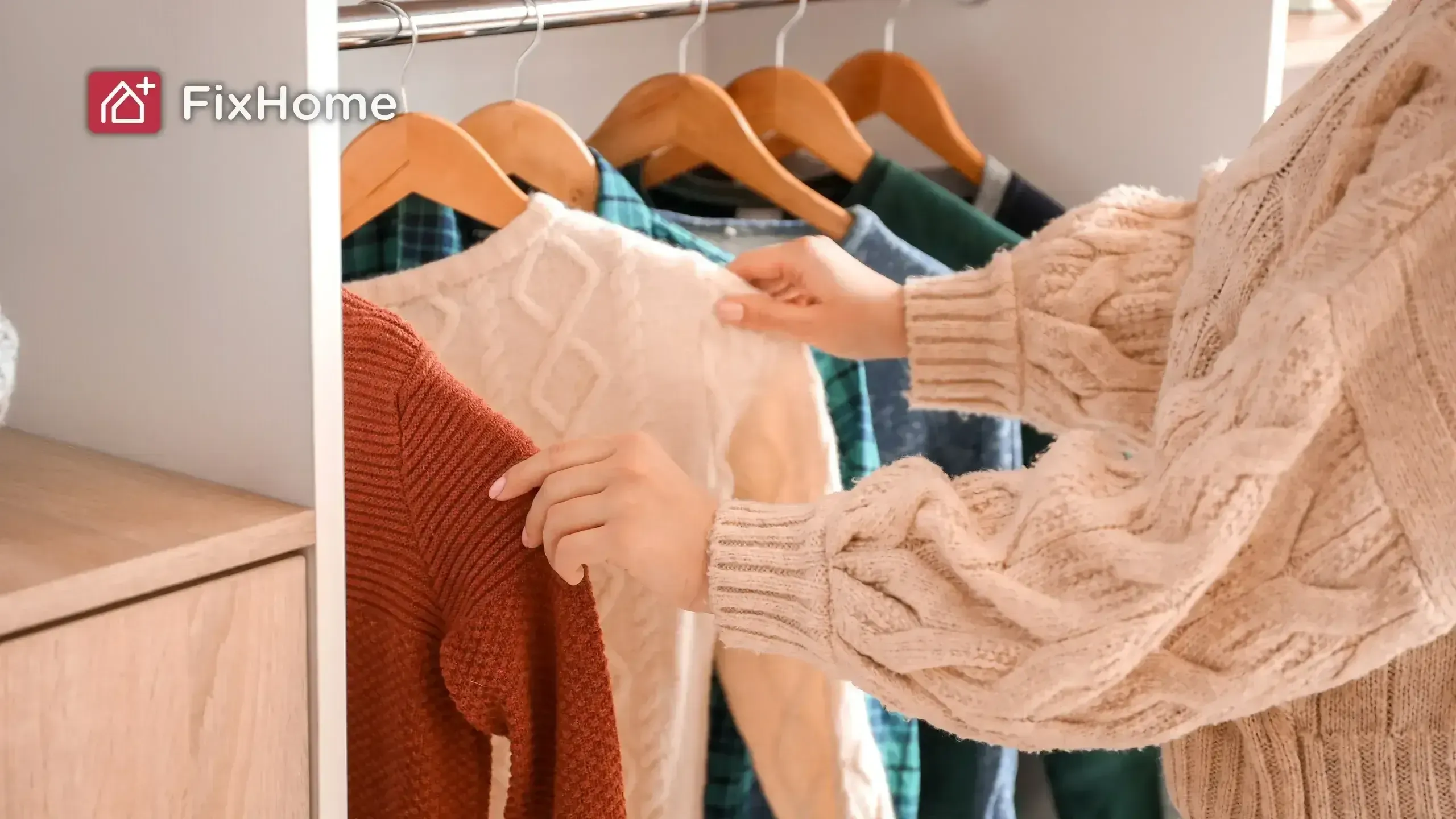 A woman in a beige sweater selects a rust-colored sweater from a closet full of sweaters