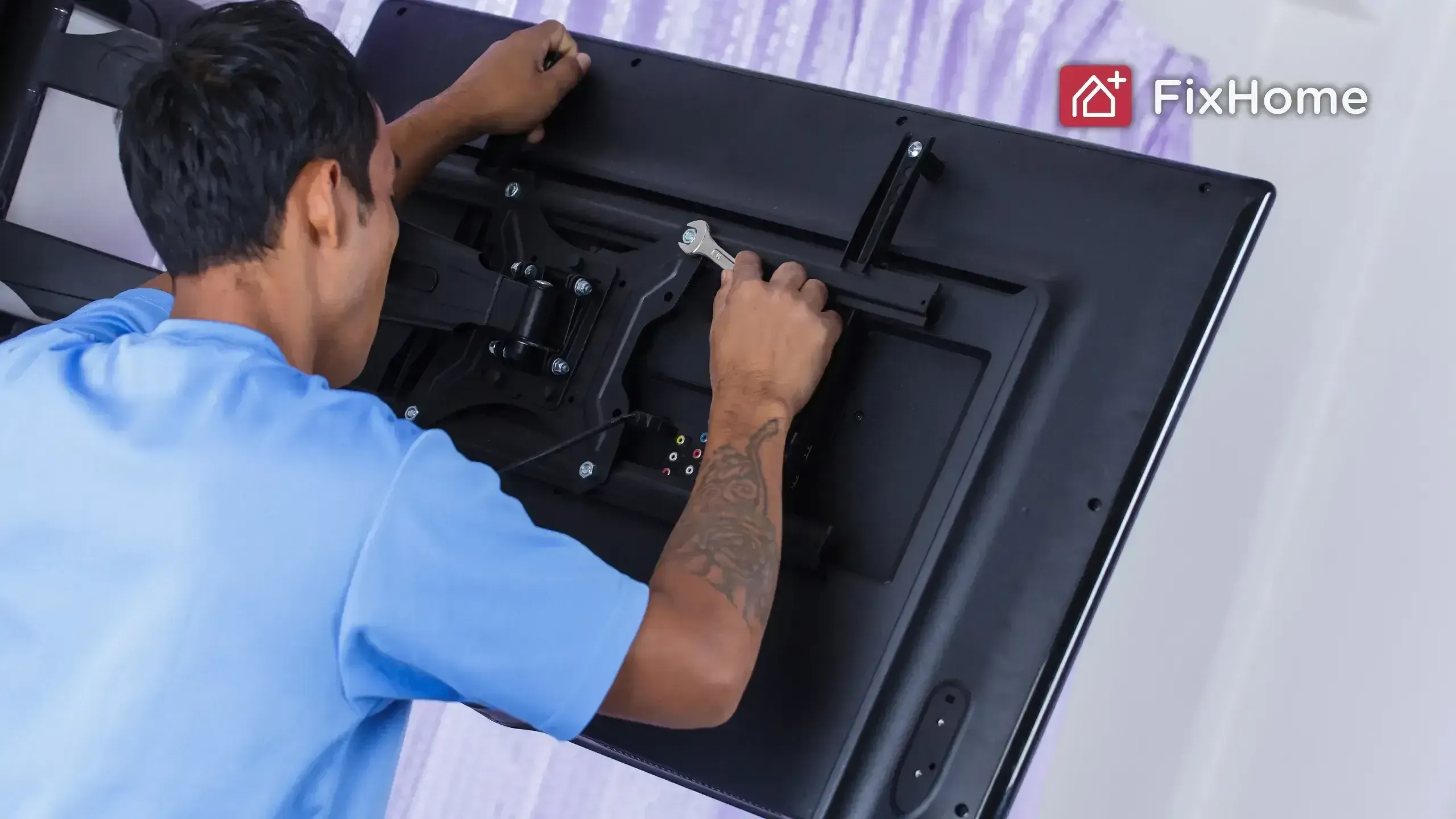 A person in a blue shirt adjusting a TV mounting bracket on the back of a large television