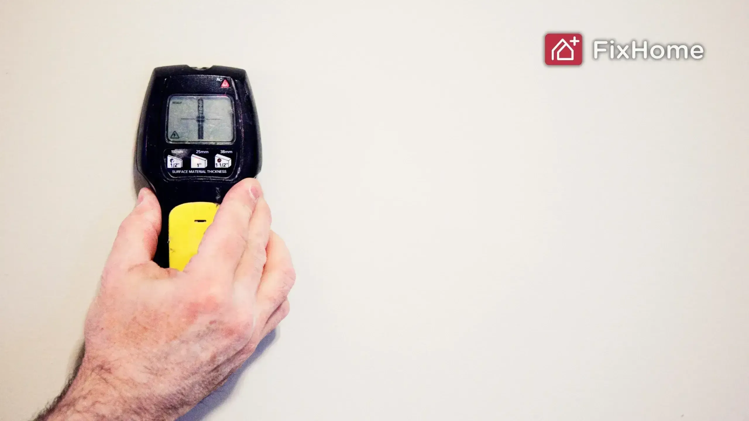 A hand with a stud finder on the wall