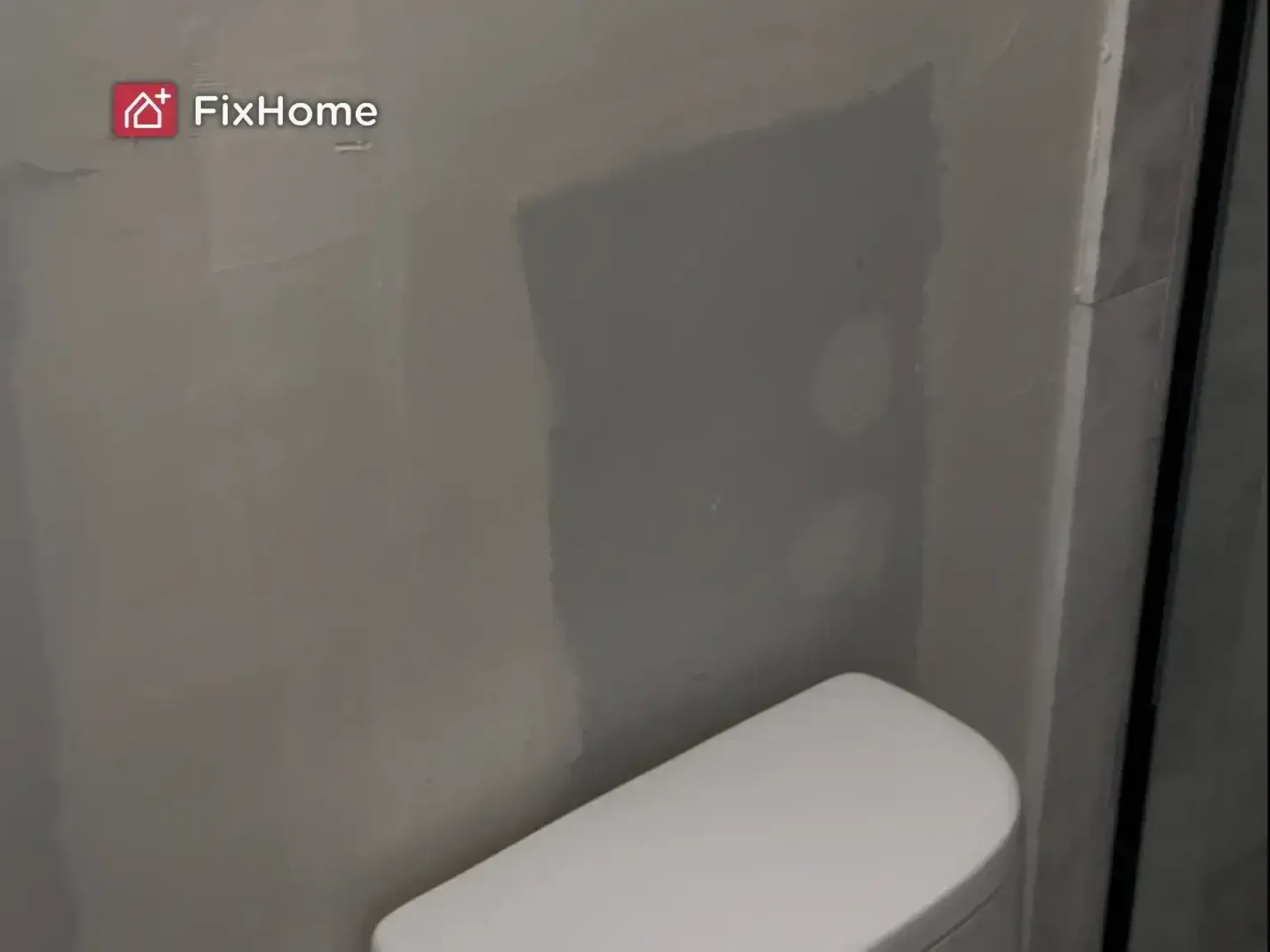 A bathroom wall before painting with gray paint patches and a white toilet in front of it.