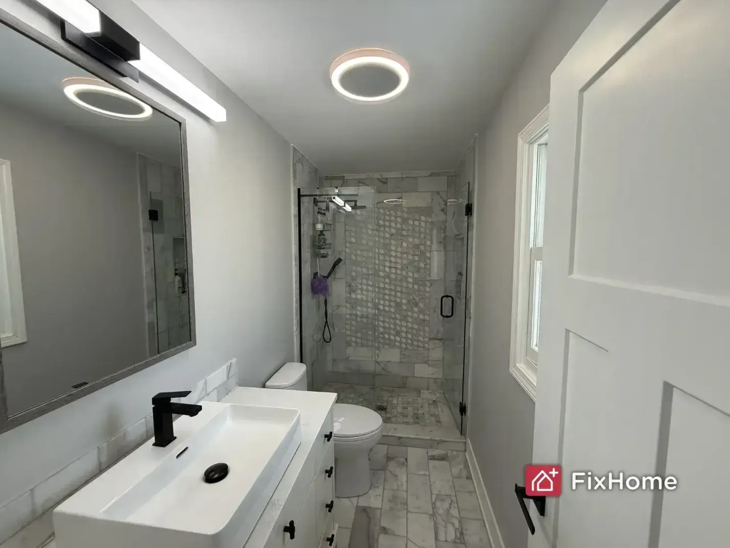 A fresh painted bathroom in Deerfield home with a black faucet, vanity, and a glass shower. Bright lighting and marble tiles