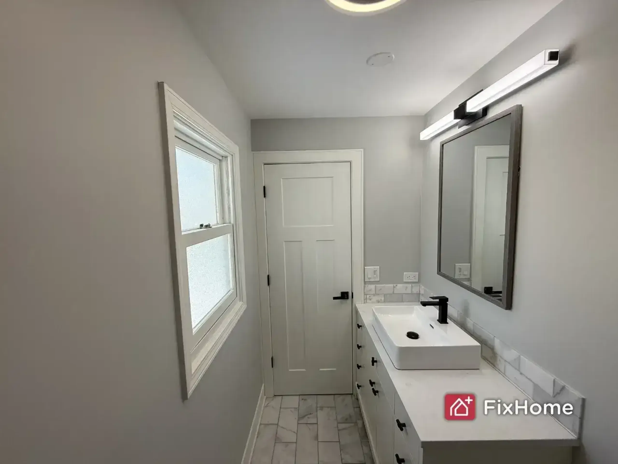 A fresh painted bathroom in the Deerfield house with a white sink, marble countertop, mirror, and window.