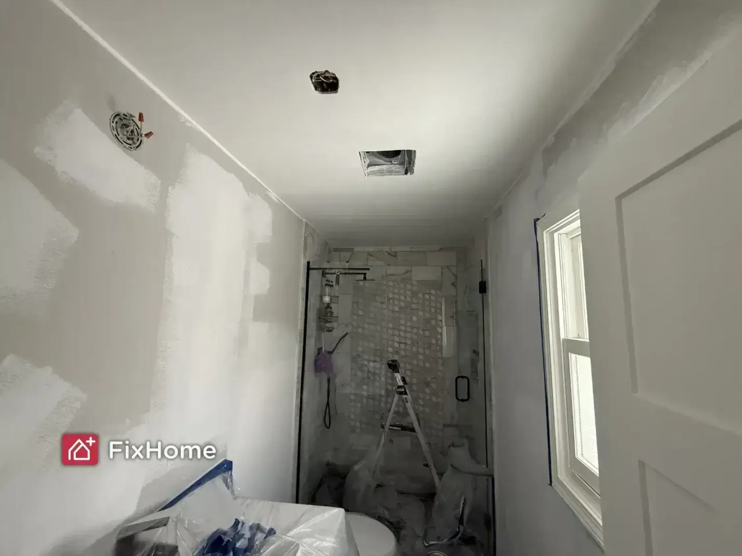 A partially painted bathroom with fresh white paint on the ceiling and a glass shower.