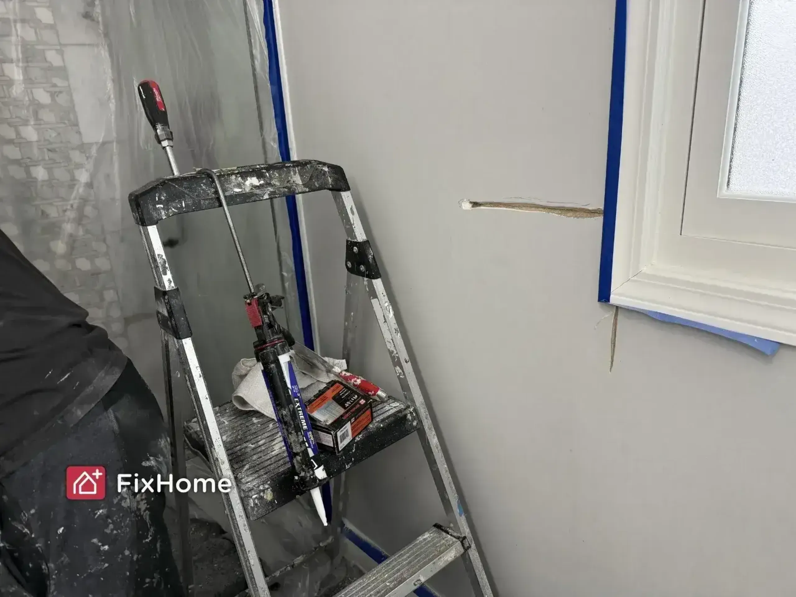 A step ladder with tools and paint supplies sits next to a wall with a large crack, ready for a bathroom painting project