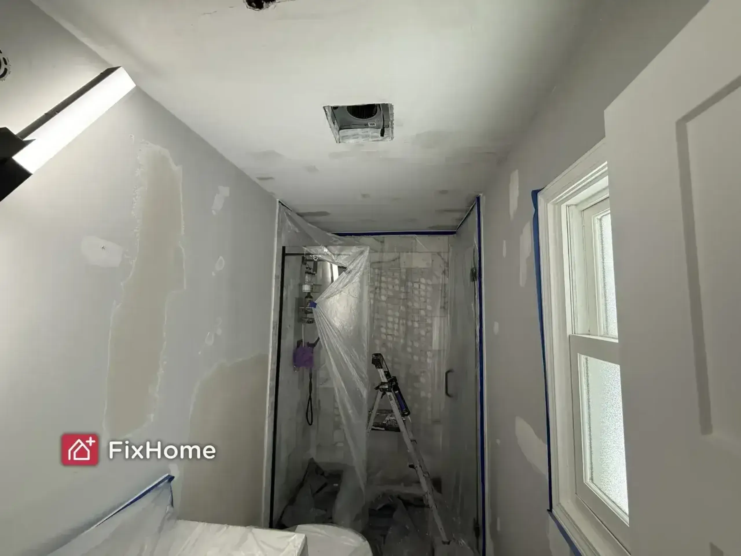 A partially renovated bathroom in the Deerfield house during the painting process with white walls, covered equipment, and a window