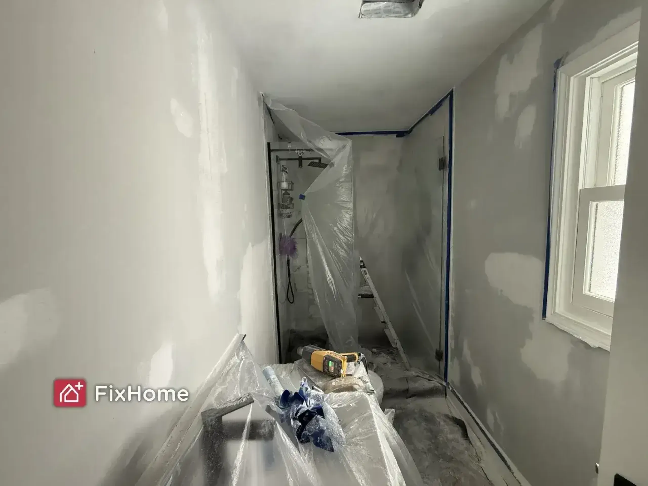 A partially renovated bathroom with covered furniture and walls being prepared for painting.