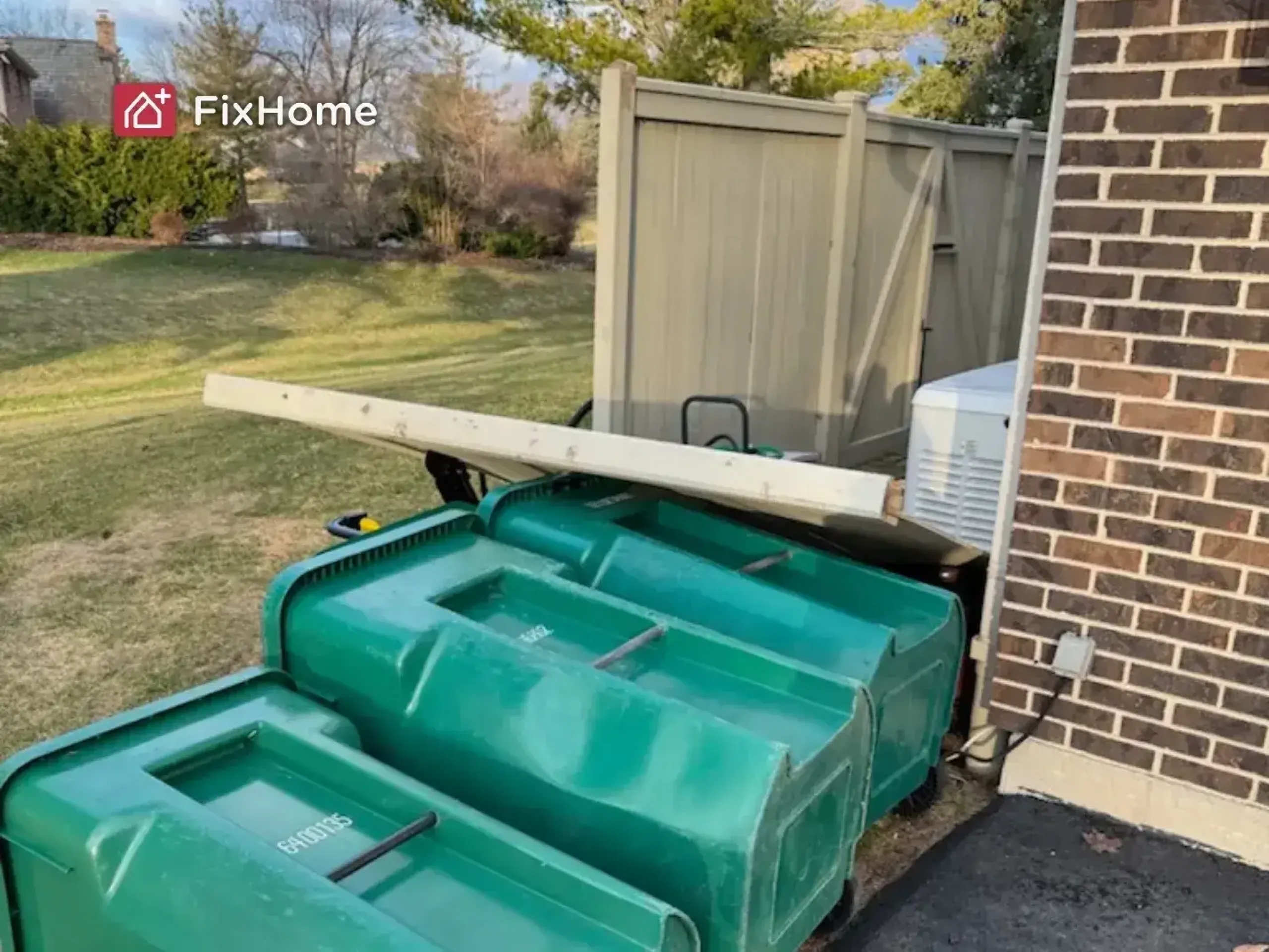 Fallen three green trash bins with a storm knocked down a fence section on top of them
