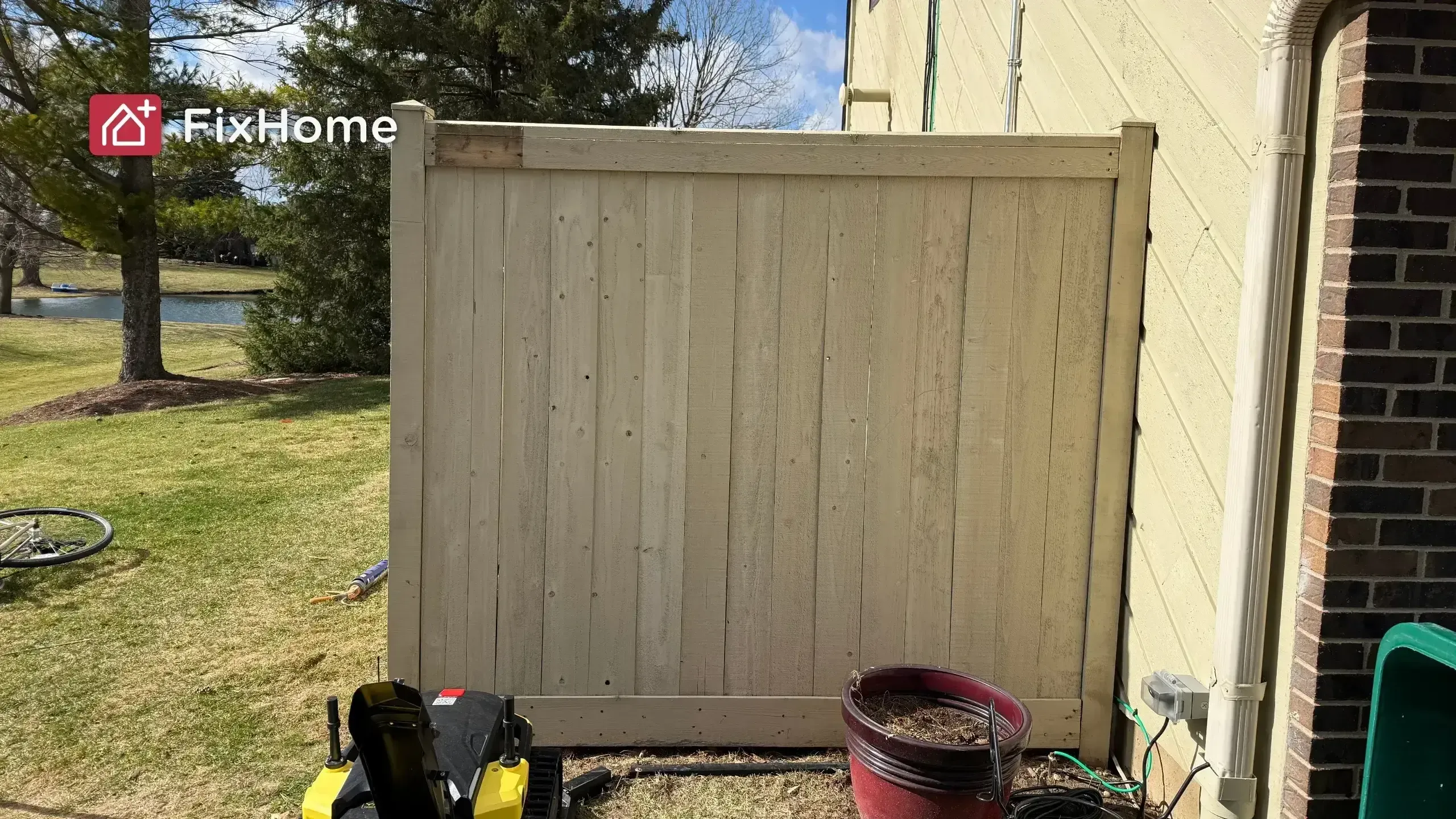 A fixed wooden fence next to a house in Hawthorn Woods, IL, with a planter and grass in the foreground, trees in the background
