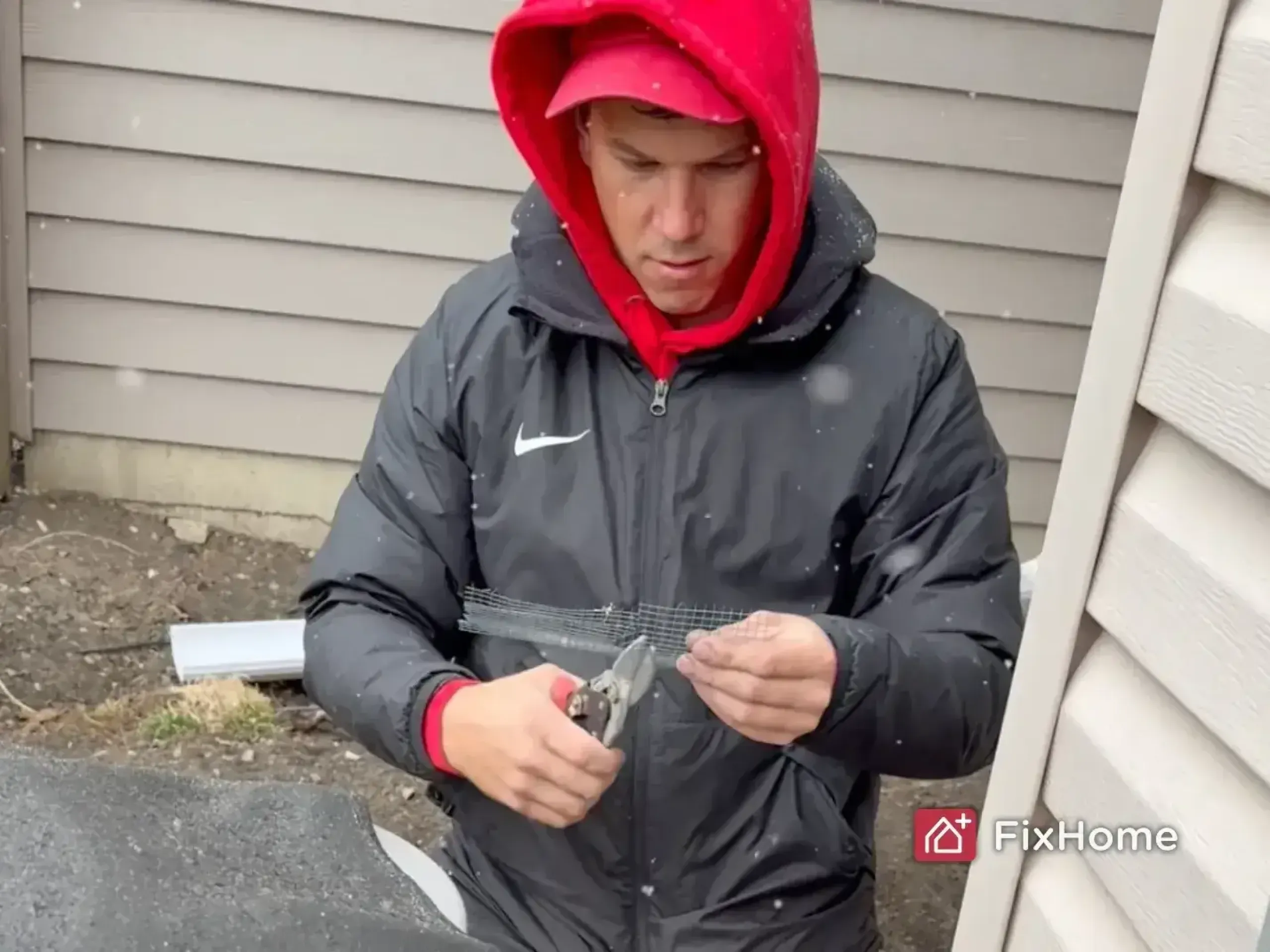 Handyman trimming galvanized hardware cloth beside a house