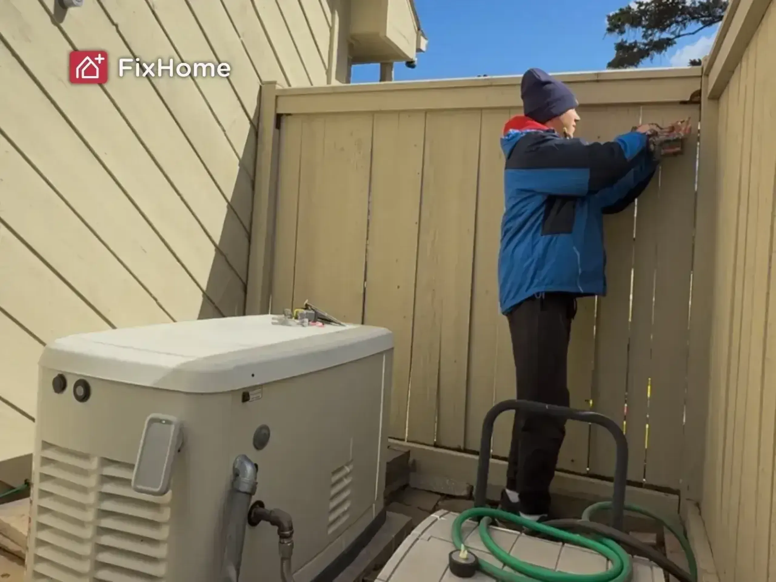 A FixHome+ handyman stands next to a repaired fence, holding a power drill