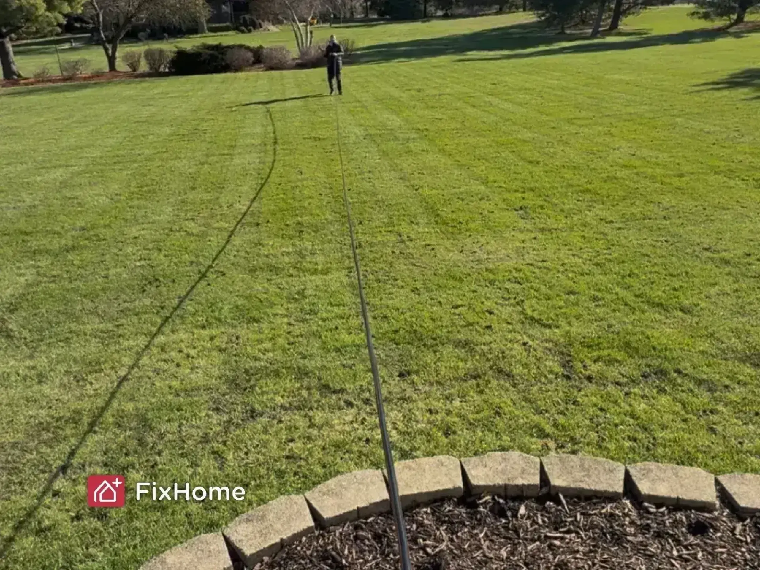 A handyman is pulling a long garden hose across a large, sunny lawn to check its length after installing the reel.