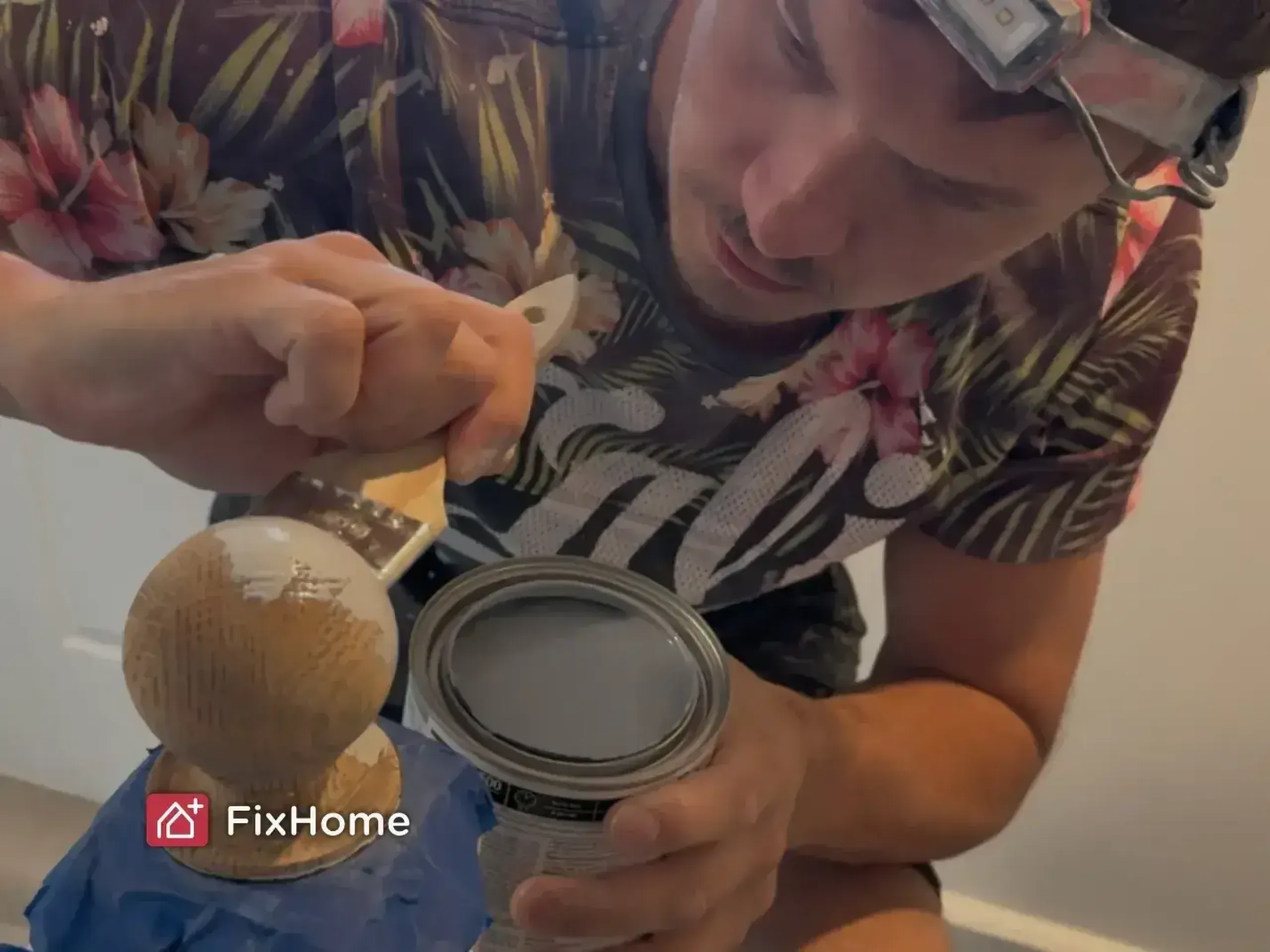 A handyman is focused on painting a wooden knob gray using a brush.