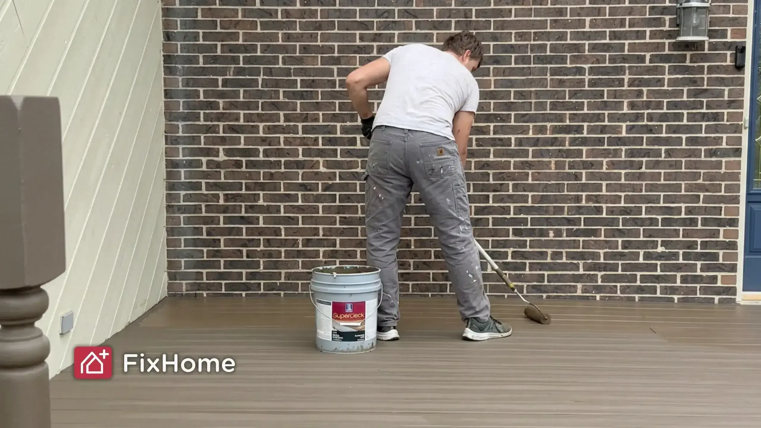 A FixHome+ handyman applying solid-color deck coating with a roller applicator on a residential deck
