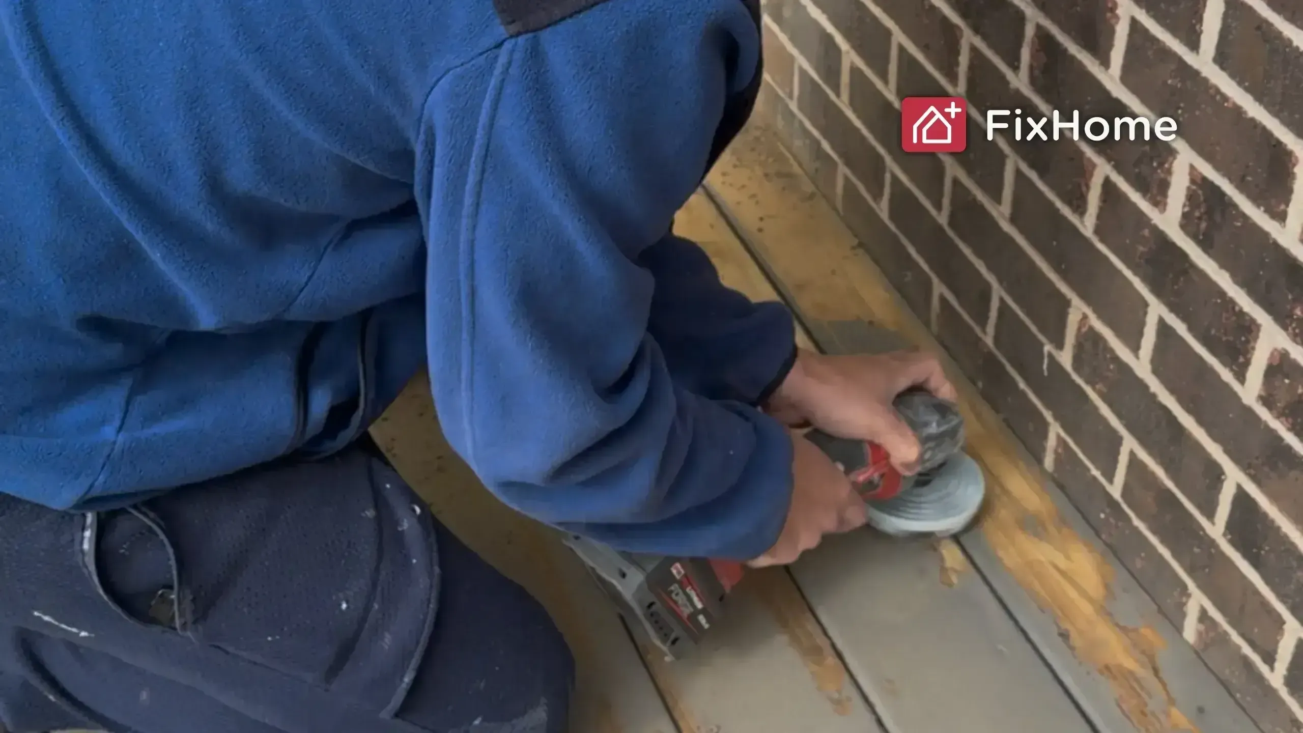Handyman stripping old paint off a wooden deck near a brick wall"