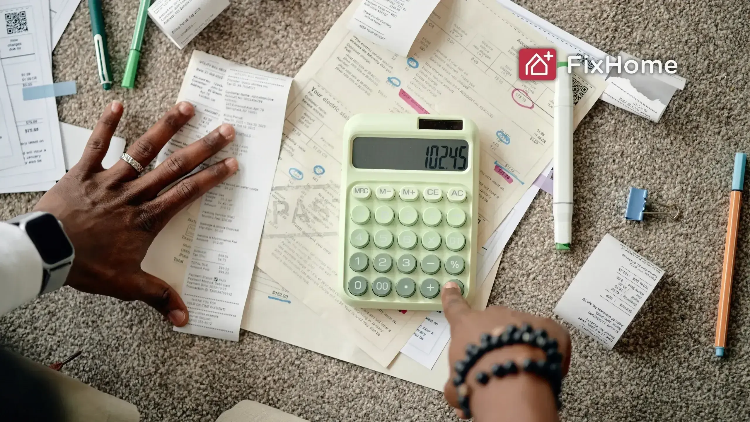 Hand calculating expenses on a green calculator surrounded by invoices and papers