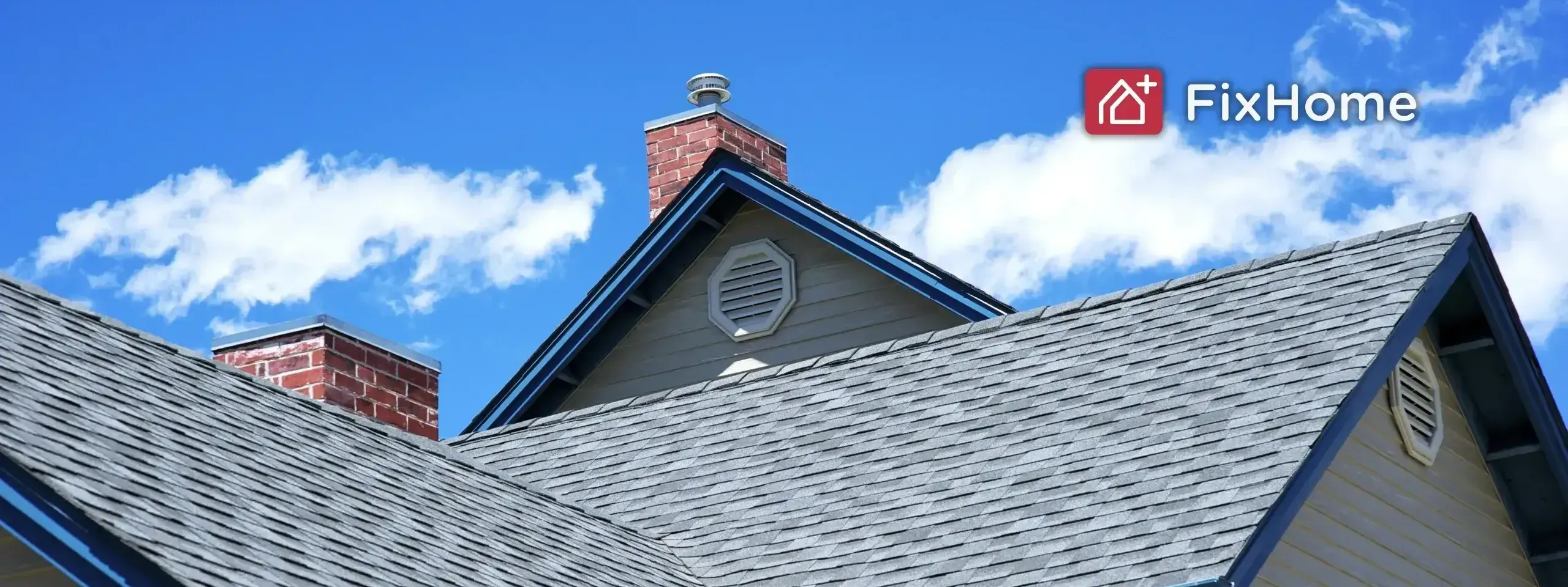 A view of a house roof with shingles and a brick chimney against a blue sky.