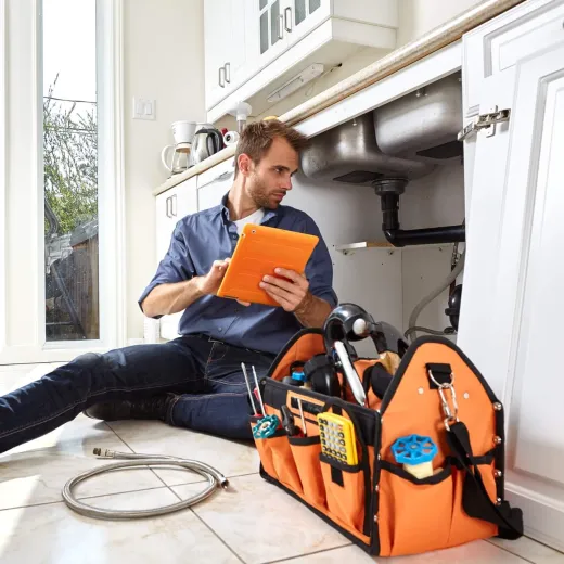 Handyman sitting on the kitchen floor resolving pipe problems