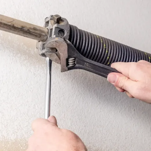 A handyman is tightening a garage door spring using a wrench and a tool in a home setting