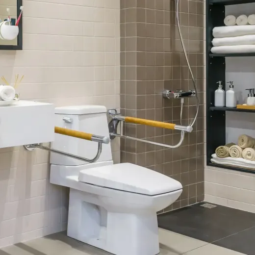 A bathroom with a toilet with handrails, sink and mirror