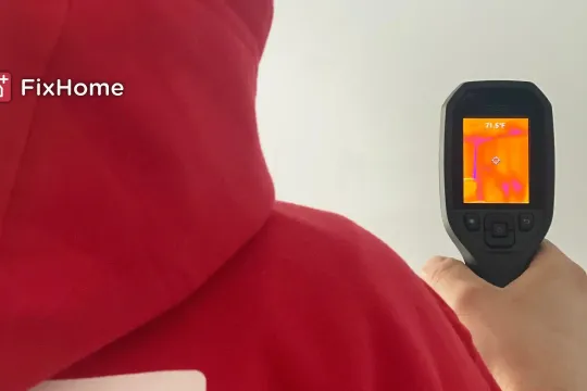 A person in a red hoodie using a thermal camera to inspect a wall
