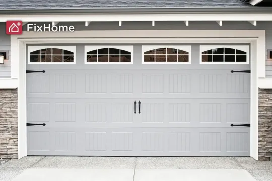 A grey garage door with decorative windows and black handles, next to stone walls. 