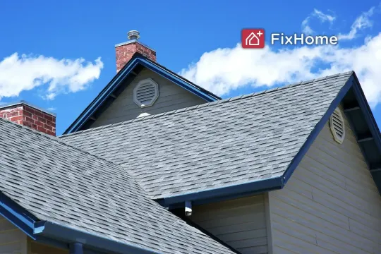 A view of a house roof with shingles and a brick chimney against a blue sky.
