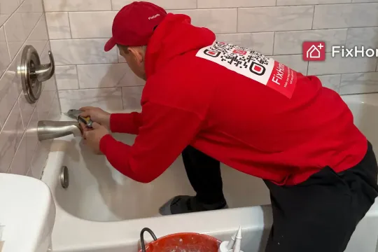 The handyman using a utility knife removes old silicone from the bathtub teaser