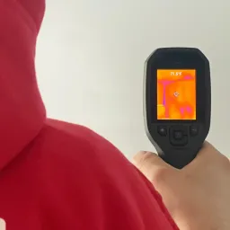 A person in a red hoodie using a thermal camera to inspect a wall