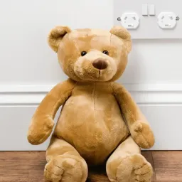 Teddy bear next to a outlet with closed protective covers