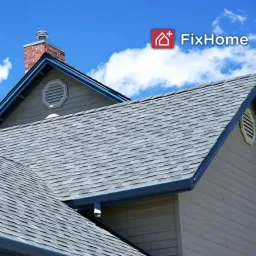 A view of a house roof with shingles and a brick chimney against a blue sky.