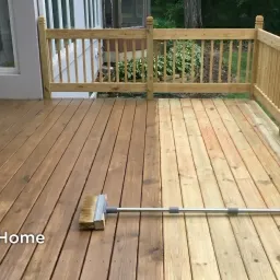 A suburban wood deck mid-staining — half the boards already stained to a warm brown, the other half still bare, with a long-handled brush resting across the work line