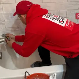 The handyman using a utility knife removes old silicone from the bathtub teaser